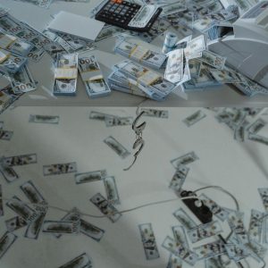 Stacks of US dollar bills scattered across a desk with a money counter and calculator.