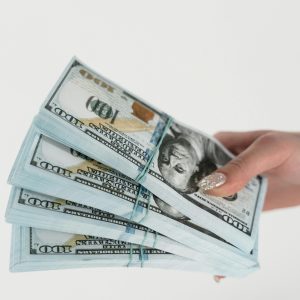 Close-up of a hand holding several stacks of US hundred dollar bills on a white background.
